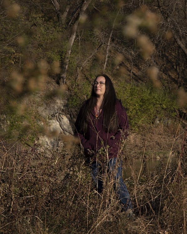 A woman standing in front of a cave reflected in water.