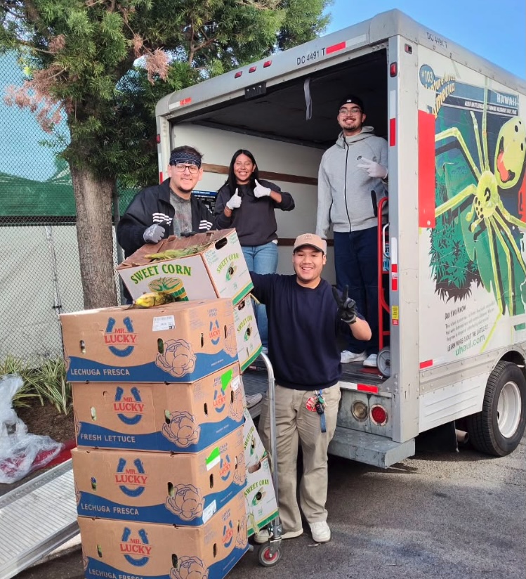 Students unload boxes of produce during a food distribution event. Four students standing at back of U-Haul truck with boxes of produce.