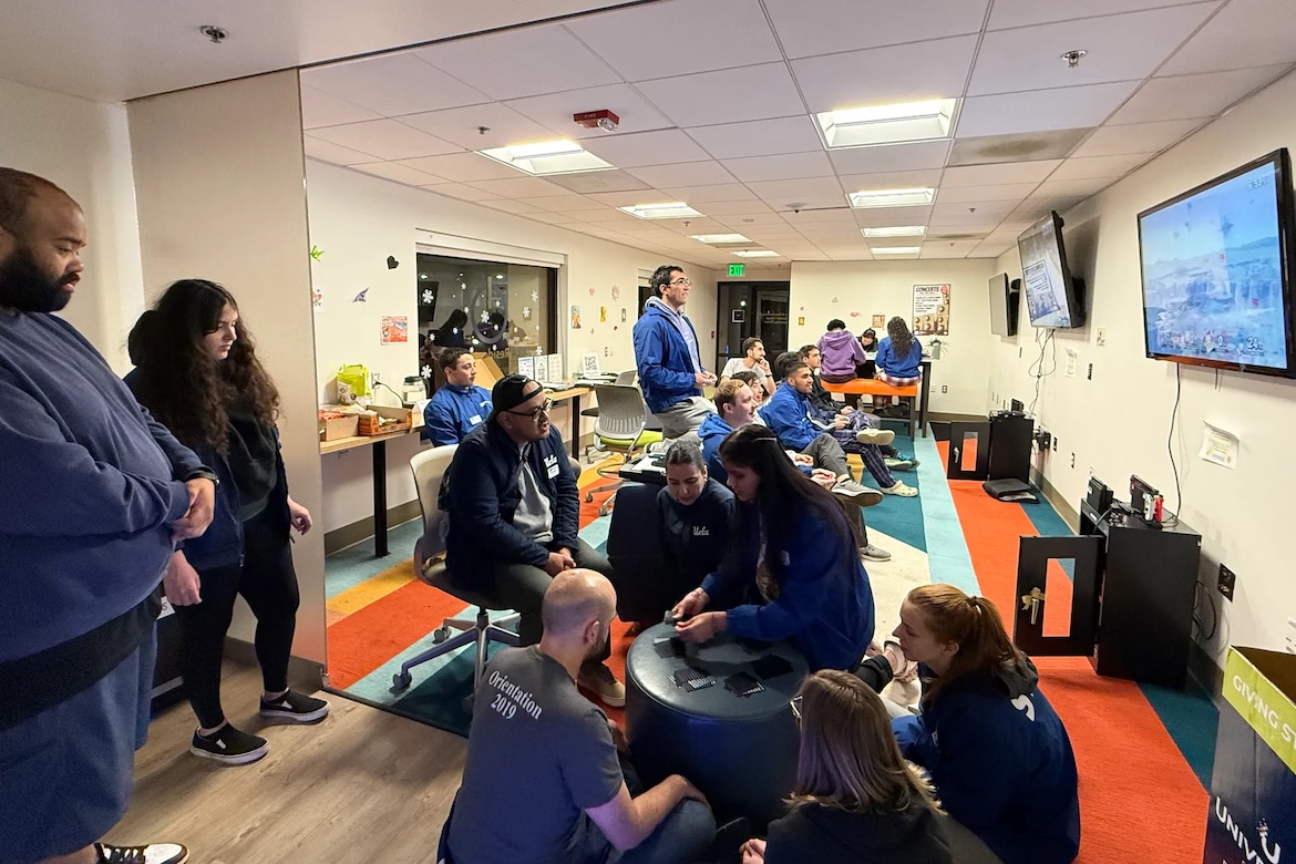 Students and Residential Life staff gather for a game night at the Sunset Village Learning Center during the fires. Group of students and Residential Life staff gathered in a room playing cards, board games and video games